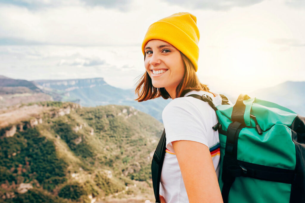 Female backpacker with mountains in the background smiling because she knows the best places to travel solo