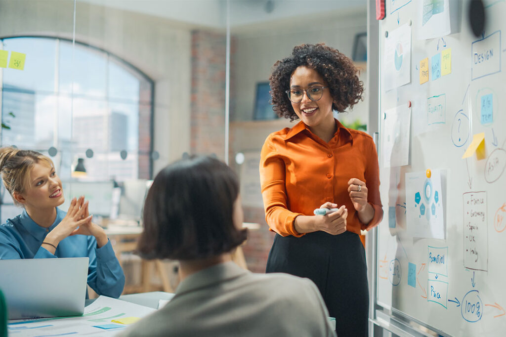 Black female businesswoman presents to a group with whiteboard