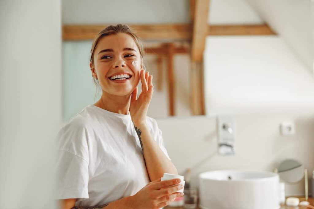 a smiling woman applying a skin care product on her face