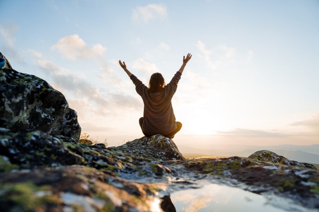 person sitting on a rock with their arms raised