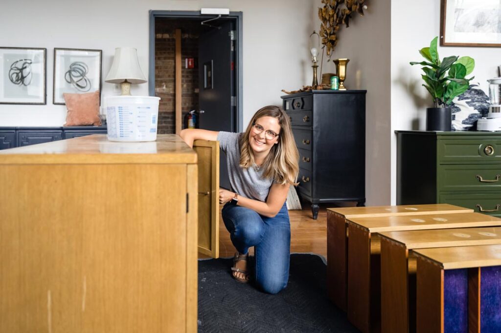 Meg Piercy host of Renovation Goldmine on HGTV kneeling in front of her MegMade furniture