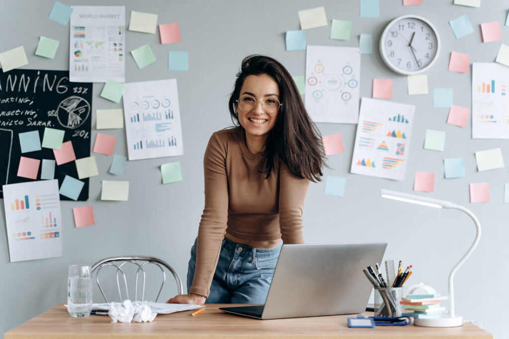 Woman at her work desk with sticky notes on the wall behind her because she's learning how to set goals at work