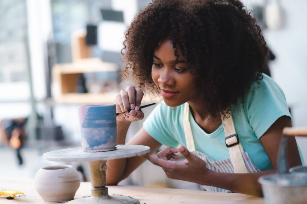 A young woman who has made time for her new hobby paints hand-made pottery in a ceramics studio.