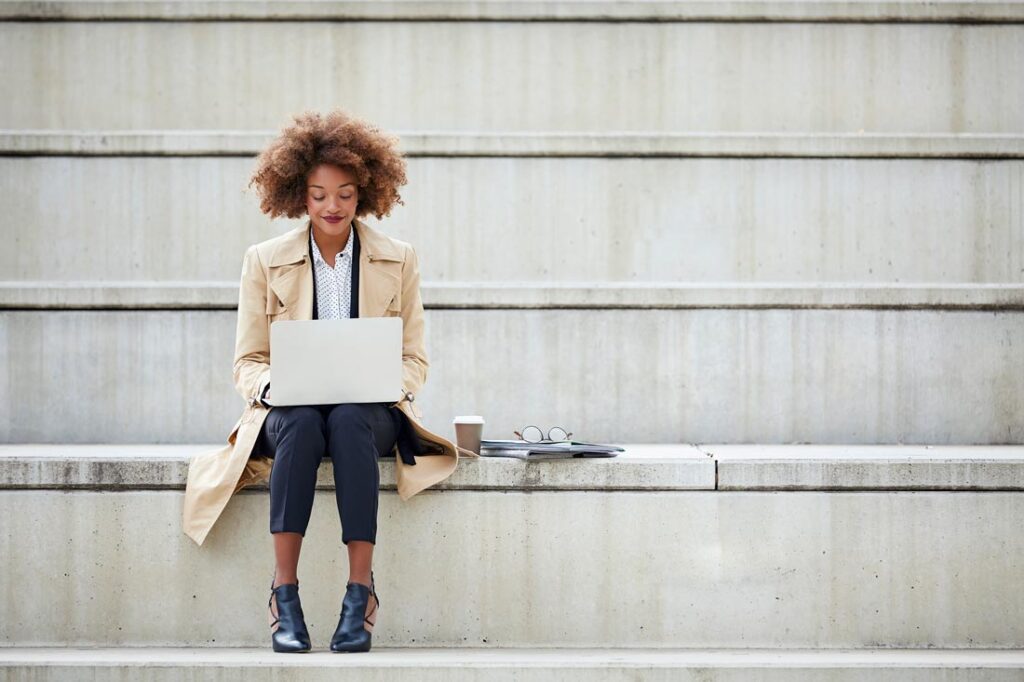 employee sitting on concrete steps working on her laptop