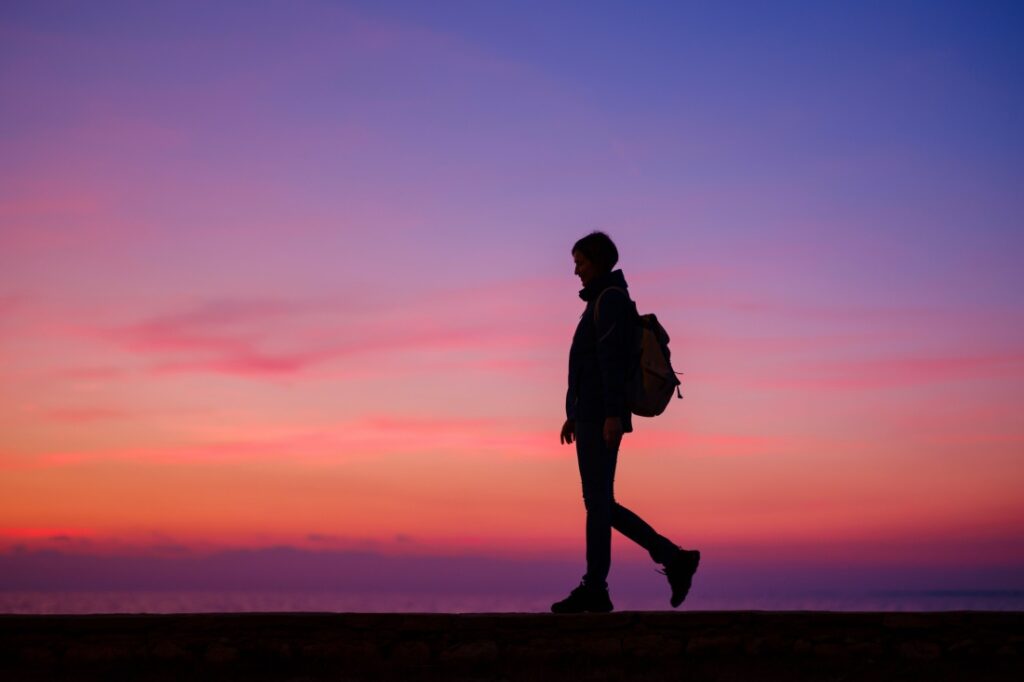 The silhouette of a woman hiking against a sunset.