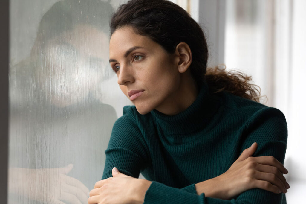 Young women stares out of a rainy window contemplating unacknowledged grief